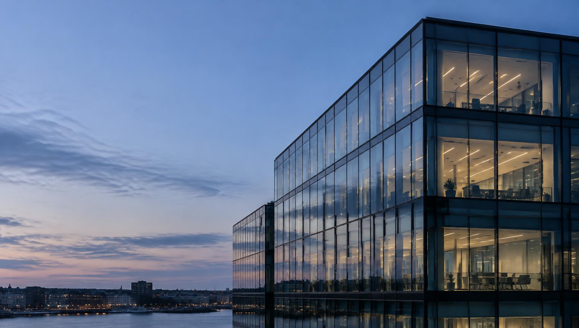 Glass office building at dusk overlooking a waterfront